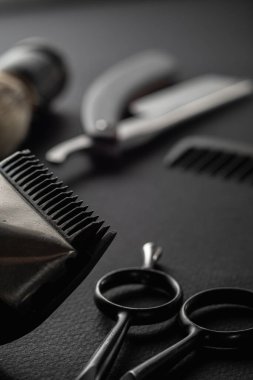 Siyah bir yüzeyde eski berber aletleri vardır. İki klasik manuel saç makası, tarak, jilet, tıraş fırçası, kuaför makası. siyah monokrom. düşey yönelim.