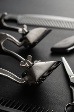 Siyah bir yüzeyde eski berber aletleri vardır. İki klasik manuel saç makası, tarak, jilet, tıraş fırçası, kuaför makası. siyah monokrom. düşey yönelim.