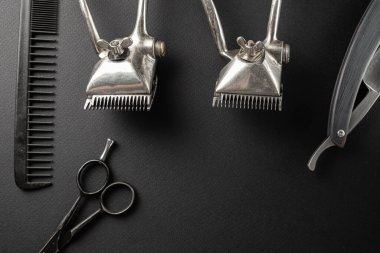 Siyah bir yüzeyde eski kuaför aletleri vardır. İki klasik el yapımı saç makası, tarak, jilet, kuaför makası, tıraş fırçası. siyah monokrom. yatay oryantasyon. Üst görünüm, düz uzanma