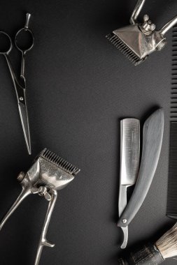 Siyah bir yüzeyde eski kuaför aletleri vardır. İki klasik el yapımı saç makası, tarak, jilet, kuaför makası, tıraş fırçası. siyah monokrom. dikey yönelim. Üst görünüm, düz uzanma