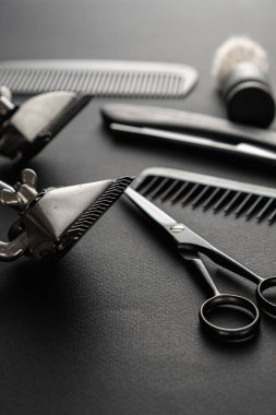 Siyah bir yüzeyde eski berber aletleri vardır. İki klasik manuel saç makası, tarak, jilet, tıraş fırçası, kuaför makası. siyah monokrom. düşey yönelim.