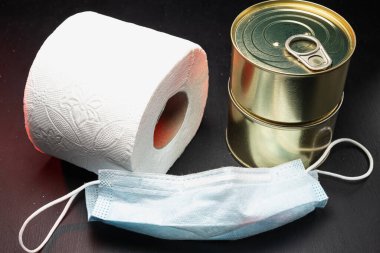 Tuvalet kağıdı rulo ve iki kutu konserve yiyecek ve tıbbi maske koronavirüs virüsü koruması kullanılmış. Dramatik. Yatay. koyu arkaplan.