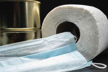 rulo tuvalet kağıdı, iki kutu konserve yiyecek ve tıbbi maske koronavirüs virüsü koruması. Yatay. Karanlık arka plan. yakın plan.