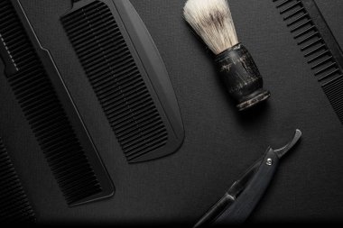 Siyah bir yüzeyde eski kuaför aletleri vardır. Taraklar, jilet, tıraş fırçası. siyah monokrom. yatay oryantasyon. Üst görünüm düz ley.