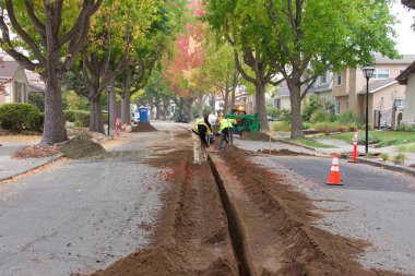 Alameda, CA - Nov 07, 2019: Crews cutting a ditch in the middle of a residential street to underground lines for street lights. Undergrounding is critical in high fire risk areas. clipart