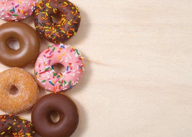 Düz görünüm çeşitli tatlar pasta donutları, fotokopi alanı ile açık ahşap masa üzerinde yatıyordu.