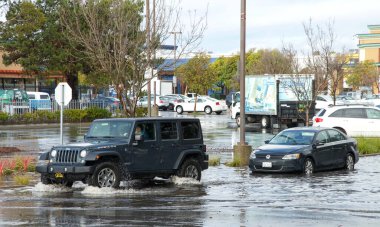Alameda, CA - Jan 16, 2020: Vehicles drive through flooded road despite flood warning signs. It is recommended not to stop in the middle of flooded road to prevent water damage and stalling of vehicle clipart