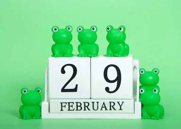 White calendar blocks February 29 on green background with generic green frogs on and around calendar. Leap Year theme