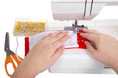 Ellerinizi yakın tutun, cerrahi stil yüz maskesi yapın. İyi kullanılmış bir dikiş makinesinde, parlak kırmızı ve beyaz pamuk kumaşlardan filtre cebi yapın. Beyazda izole edilmiş.