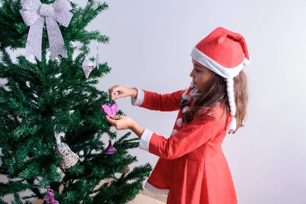 En liten flicka som dekorerar julgranen. Förklädd till jultomten. — Stockfoto