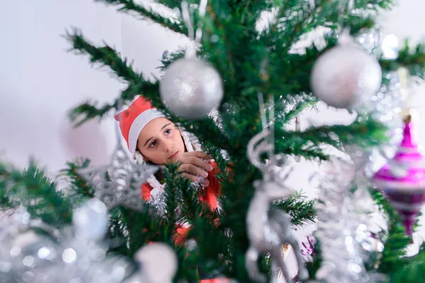 En liten flicka som dekorerar julgranen. Förklädd till jultomten. — Stockfoto