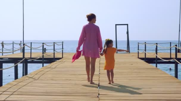 Mother and daughter walk along the pier on the sea coast and admire the sea. — Stock Video