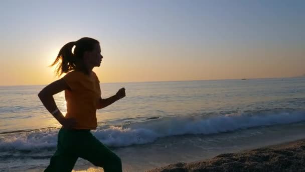 Eine junge Frau joggt am Sandstrand entlang. — Stockvideo
