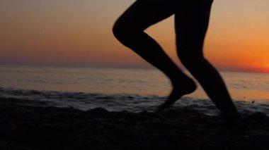 Kumlu sahil boyunca koşan genç bir kadın..