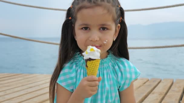 Little girl licks ice cream cone on a background of sea or ocean. — Stock Video