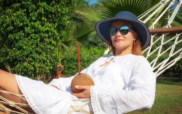 Genç bir kadın elinde hindistan cevizi suyu kokteyliyle hamakta yatıyor..