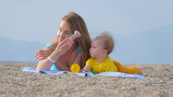 Giovane madre gioca a sonagli con il suo bambino sulla spiaggia di sabbia . — Video Stock