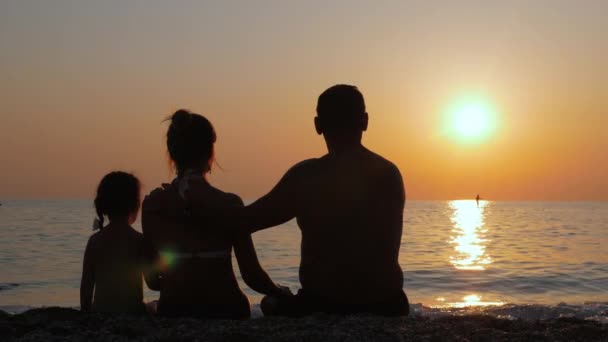 Os pais com seu filho apreciam o pôr do sol junto ao mar ou à costa oceânica . — Vídeo de Stock