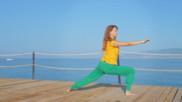 Jonge vrouw doen stretching op houten pier tegen de achtergrond van de zee of de oceaan. — Stockvideo