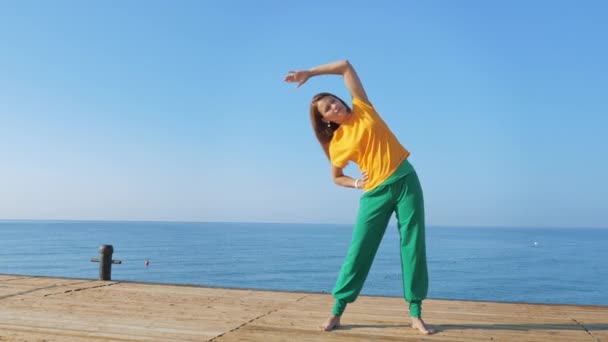 Jonge vrouw doen stretching op houten pier tegen de achtergrond van de zee of de oceaan. — Stockvideo