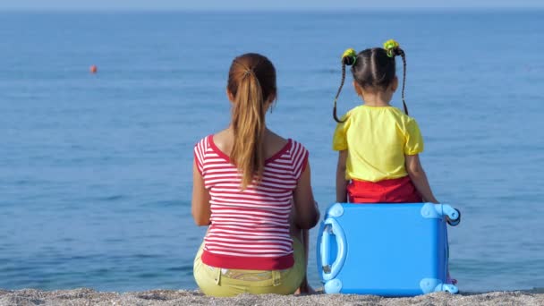 Pequeña linda chica y su mamá en ropa de colores están sentados en la playa . — Vídeos de Stock