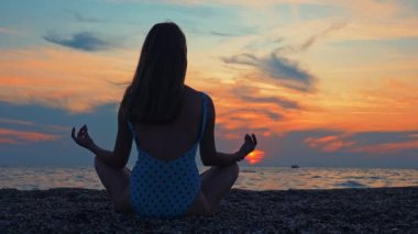 Genç kadınlar gün batımında deniz kenarında ya da okyanusta yoga yaparlar..