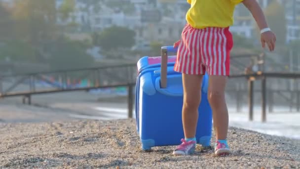 Den lille søte jenta går med en koffert på en feriestrand. . – stockvideo