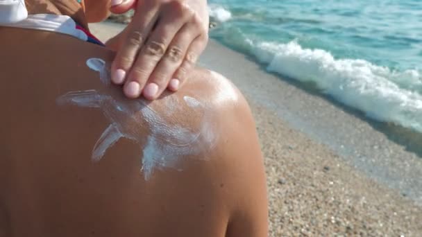 Дівчина мазає плече сонячним кремом, стоячи на гальковому пляжі . — стокове відео