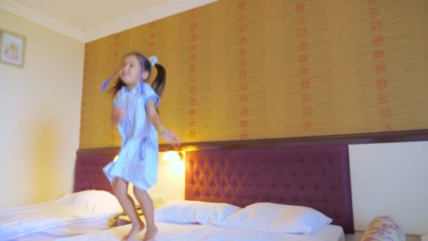 Uma menina salta na cama em um quarto de hotel, se diverte e gosta da vida . — Vídeo de Stock