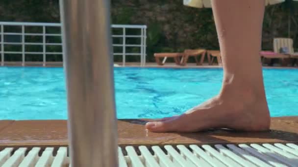 Een meisje met blote voeten loopt langs de rand van een zwembad van blauw helder water. — Stockvideo