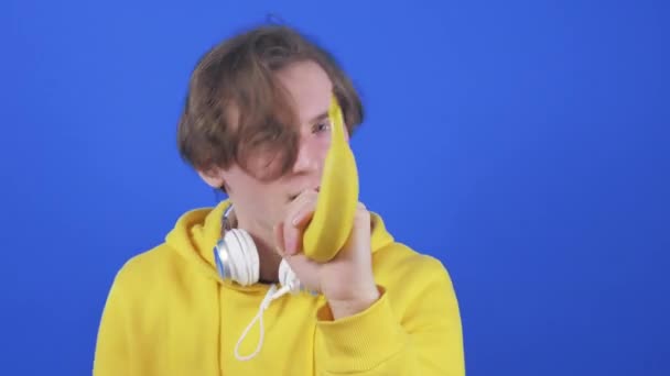 Молодой человек в толстовке поет в банане на синем фоне . — стоковое видео