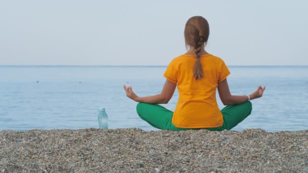 Une jeune femme en vêtements colorés pratique le yoga au bord de la mer ou de l'océan . — Video