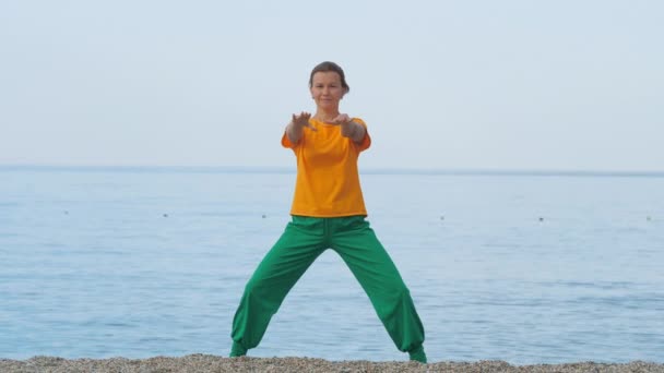 Mujer joven haciendo estiramiento en una playa de arena contra el fondo del mar o el océano . — Vídeos de Stock