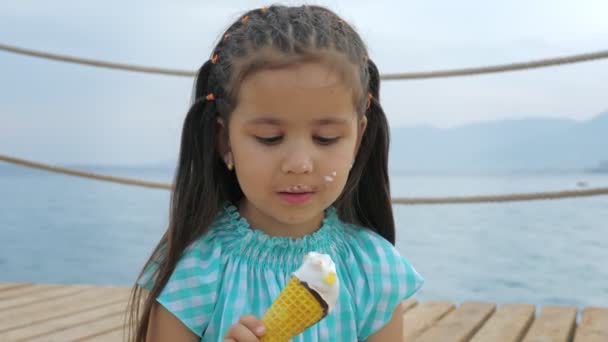 Malá dívka olizuje zmrzlinu kornout na pozadí moře nebo oceánu.