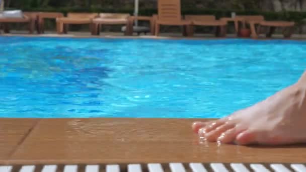 Een meisje met blote voeten loopt langs de rand van een zwembad van blauw helder water. — Stockvideo