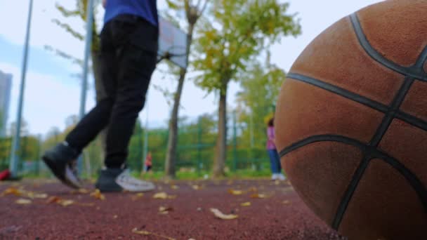 Um cara e uma menina jogam um basquete em uma cesta em um playground . — Vídeo de Stock