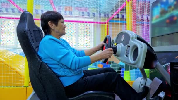 सीनियर महिला कार सिम्युलेटर पर सवारी करते समय मज़ा कर रही है — स्टॉक वीडियो