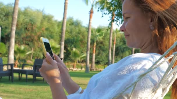 Mujer alegre usando teléfono inteligente en el jardín en verano — Vídeos de Stock