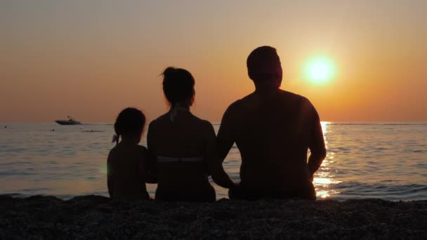 Ebeveynler çocuklarıyla birlikte deniz ya da okyanus kıyısında gün batımının tadını çıkarırlar.. — Stok video