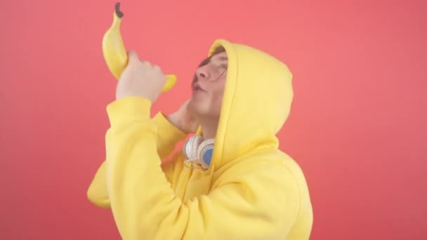 Ein junger Mann im Sweatshirt singt in einer Banane auf rotem Hintergrund — Stockvideo