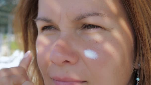 Menina esfrega a pele do rosto com creme protetor solar enquanto está em pé em uma praia — Vídeo de Stock