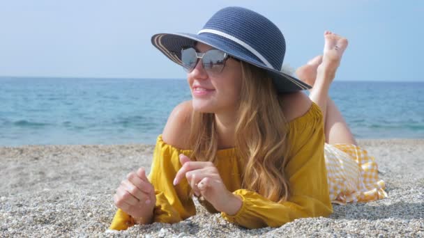 Turista femenina positiva en gafas de sol y sombrero en playa de mar — Vídeos de Stock