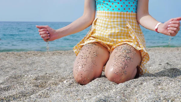 Anonymous resting lady with pebbled sand on legs and in hands on seaside