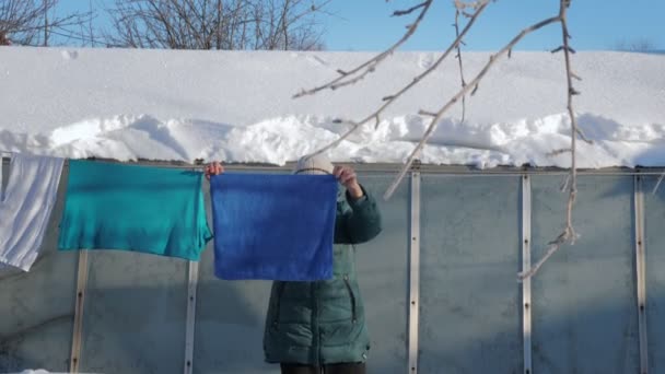 Señora mayor en ropa de abrigo colgando ropa al aire libre en invierno — Vídeos de Stock