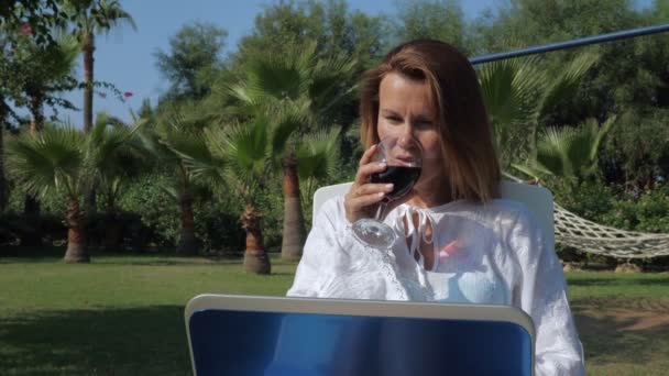 Zufriedene Freiberuflerin mit Laptop und Glas Wein im Urlaub — Stockvideo