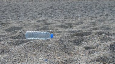 Küçük kız kumlu deniz sahilinden plastik çöpleri topluyor.