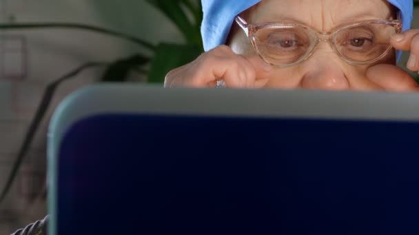 An elderly woman with glasses uses a laptop. — 图库视频影像