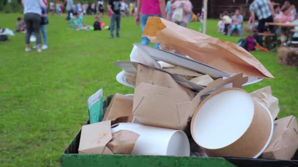 Basura de plástico y papel en un contenedor lleno de gente en el parque junto a la cafetería . — Vídeos de Stock