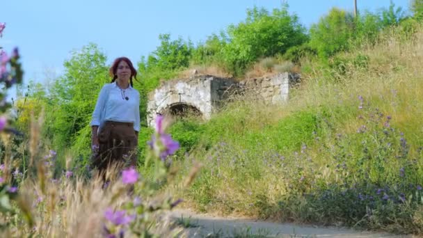 A red-haired country girl walks along a dirt road or path in the countryside. — Stockvideo