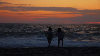 İki küçük kız gün batımında denizin ya da okyanusun kenarında durur..